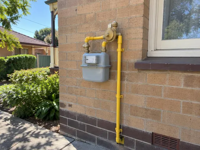 Yellow gas meter and pipework on a brick house wall beside a window in Cabarita